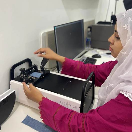 A person in a pink shirt and white head scarf working on a machineDescription automatically generated
