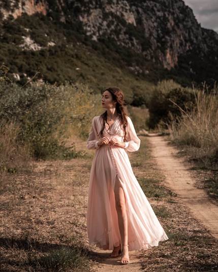 A person in a dress standing on a dirt road in front of a mountain
Description automatically generated with low confidence